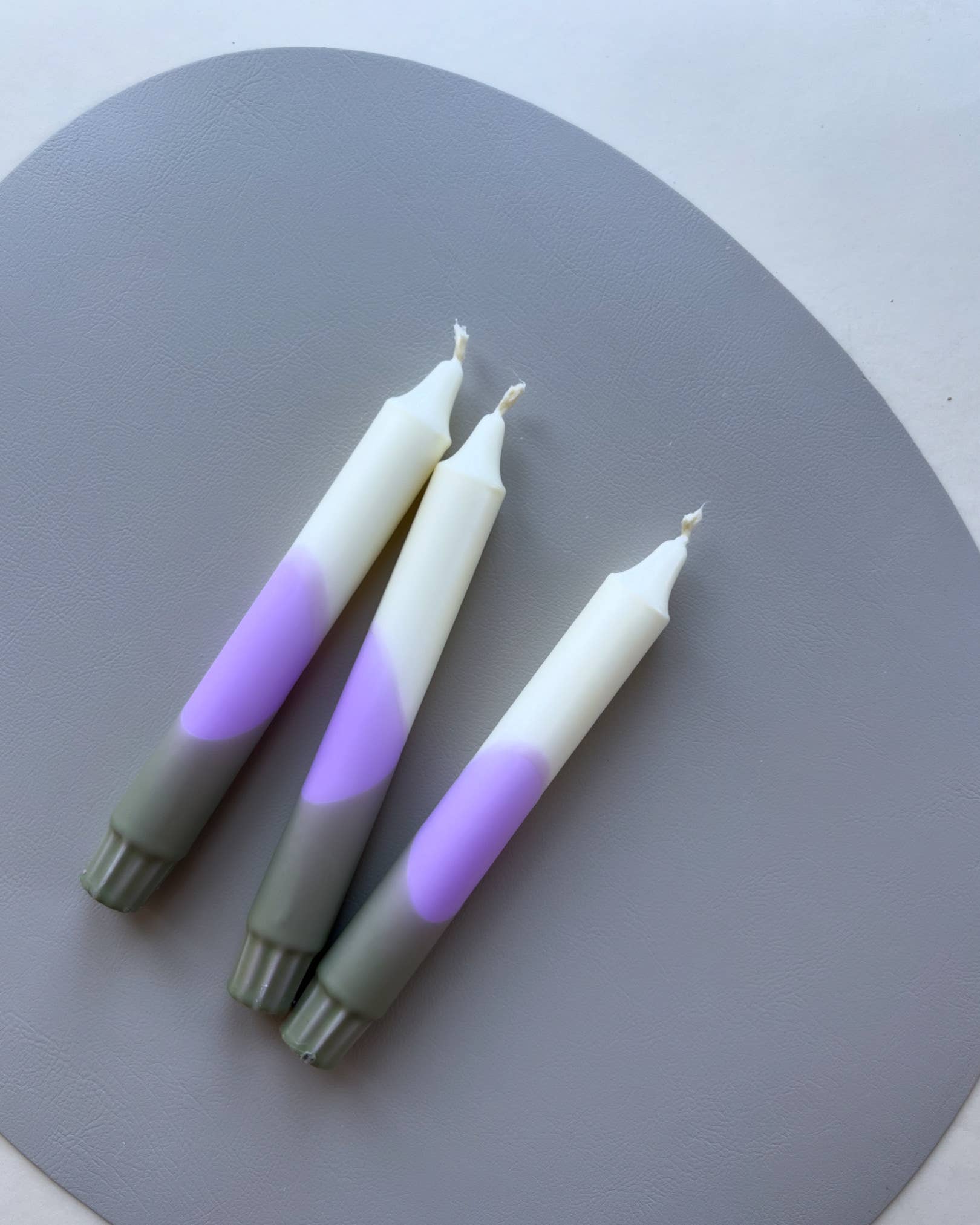 3 Dip dye kaarsen met kleurverloop in de kleuren wit, paars en olijfgroen op een grijs en witte achtergrond.