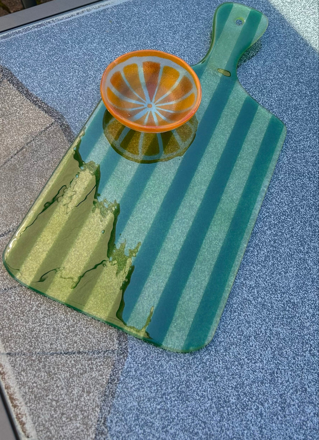Bovenaanzicht grote glazen borrelplank met groene strepen op een glazen tafel met een oranje bakje met sinaasappelpatroon erop.
