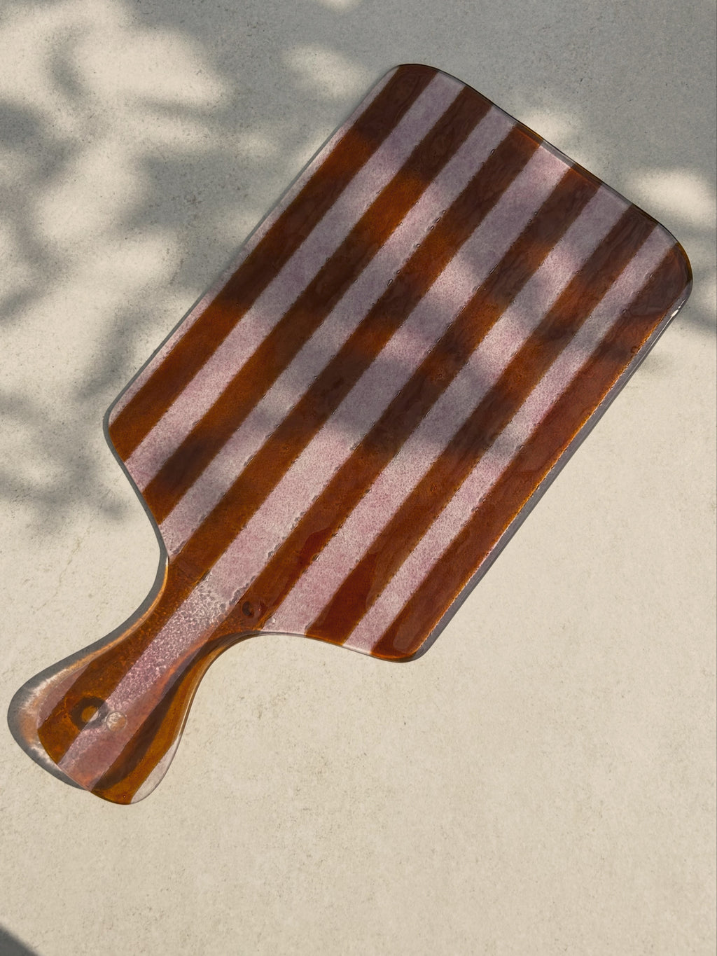 Bovenaanzicht van grote glazen borrelplank met strepen in roze tinten op een beige achtergrond.