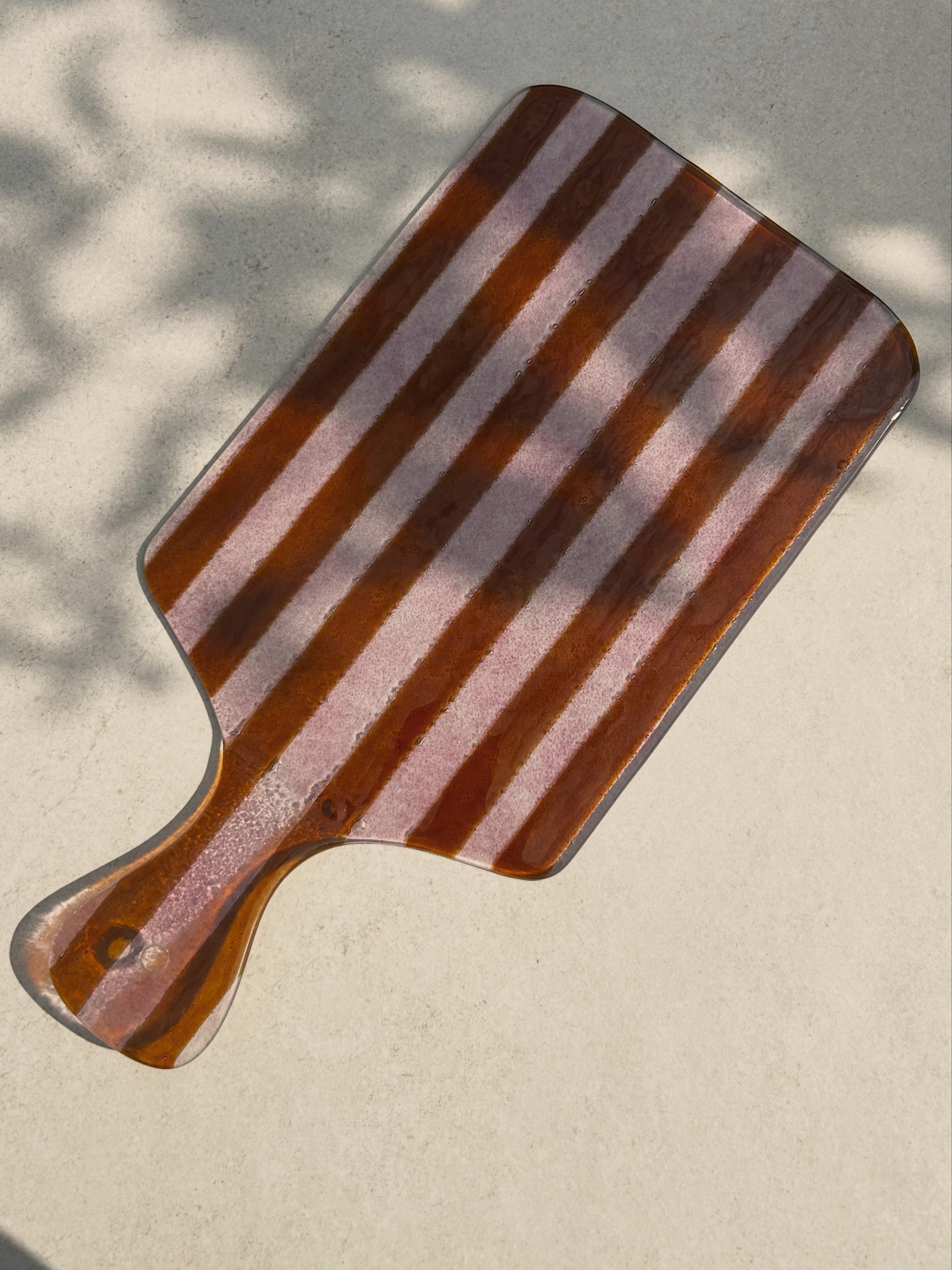 Bovenaanzicht van grote glazen borrelplank met strepen in roze tinten op een beige achtergrond.