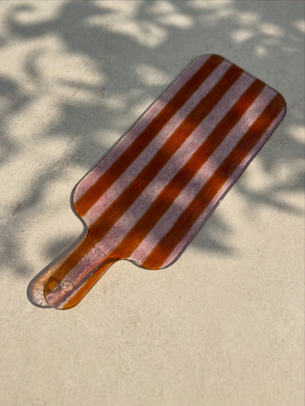 Bovenaanzicht glazen borrelplank met strepen in roze op een beige achtergrond.