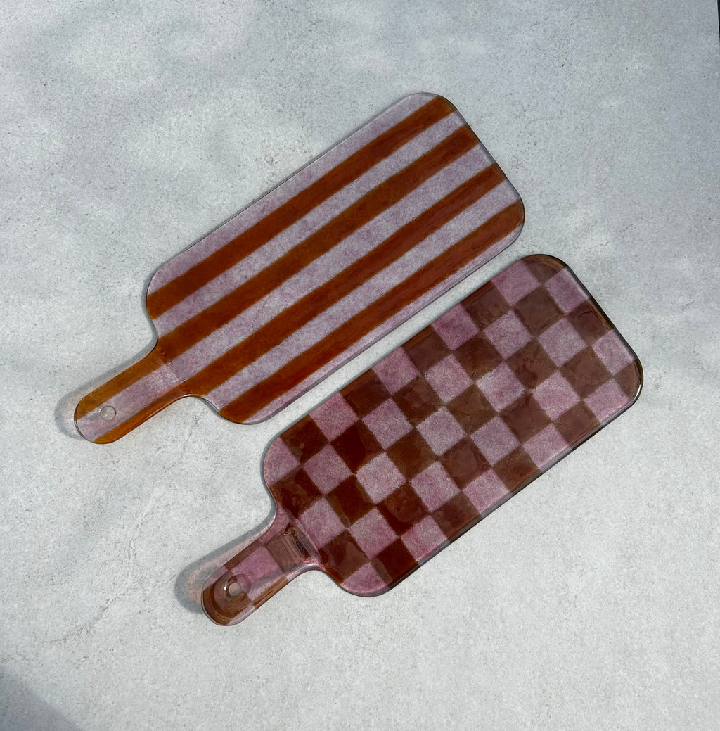 Bovenaanzicht van 2 roze glazen borrelplanken. 1 met streepjesmotief en 1 met geblokt motief op een beige achtergrond.