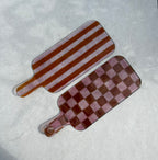 Bovenaanzicht van 2 roze glazen borrelplanken. 1 met streepjesmotief en 1 met geblokt motief op een beige achtergrond.