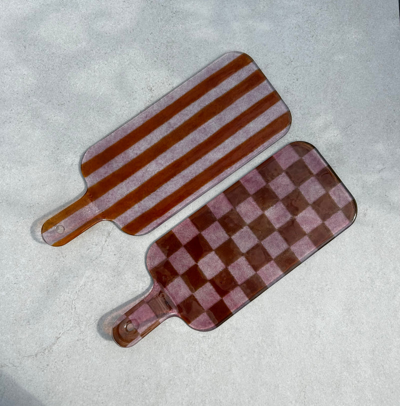Bovenaanzicht van 2 roze glazen borrelplanken. 1 met streepjesmotief en 1 met geblokt motief op een beige achtergrond.