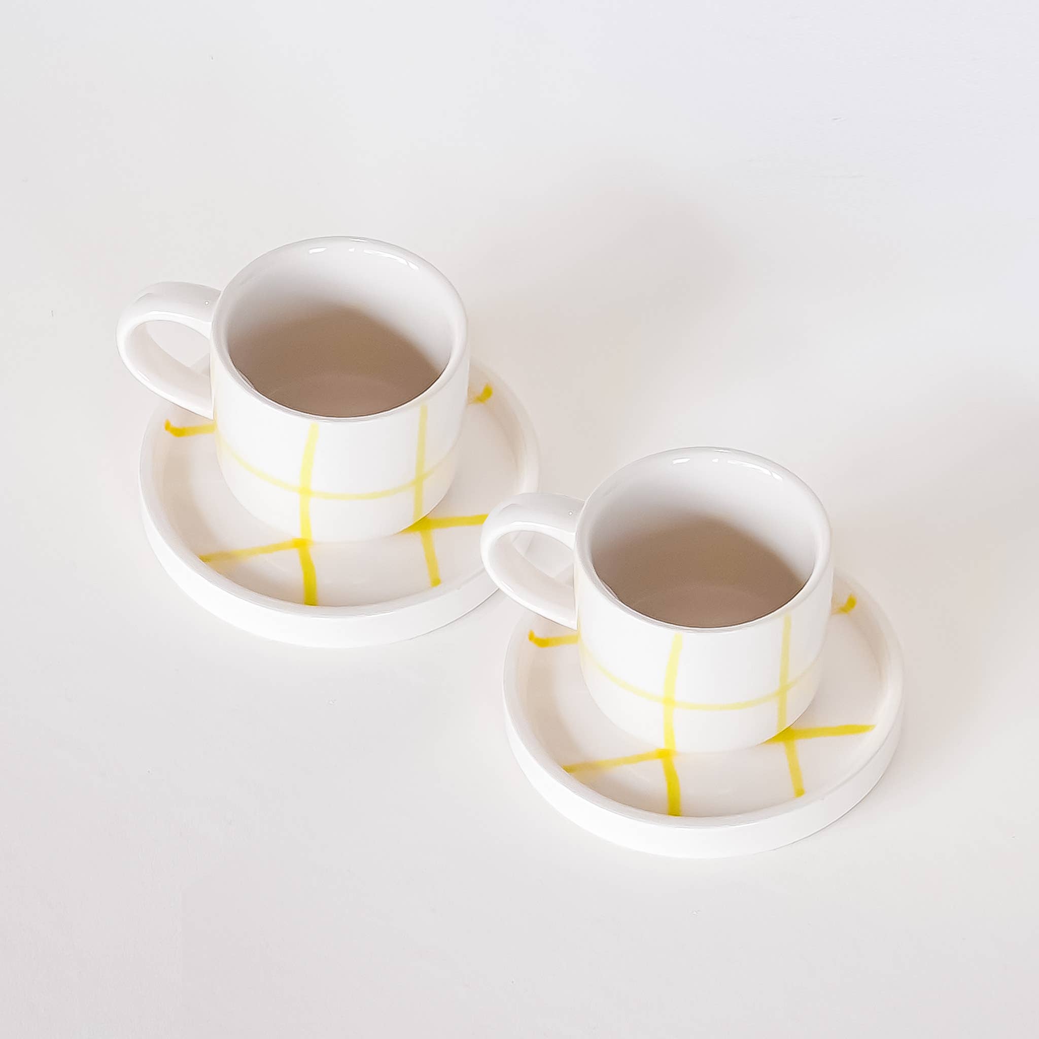 twee espresso kop en schotel in wit met een geel raster patroon op een witte achtergrond