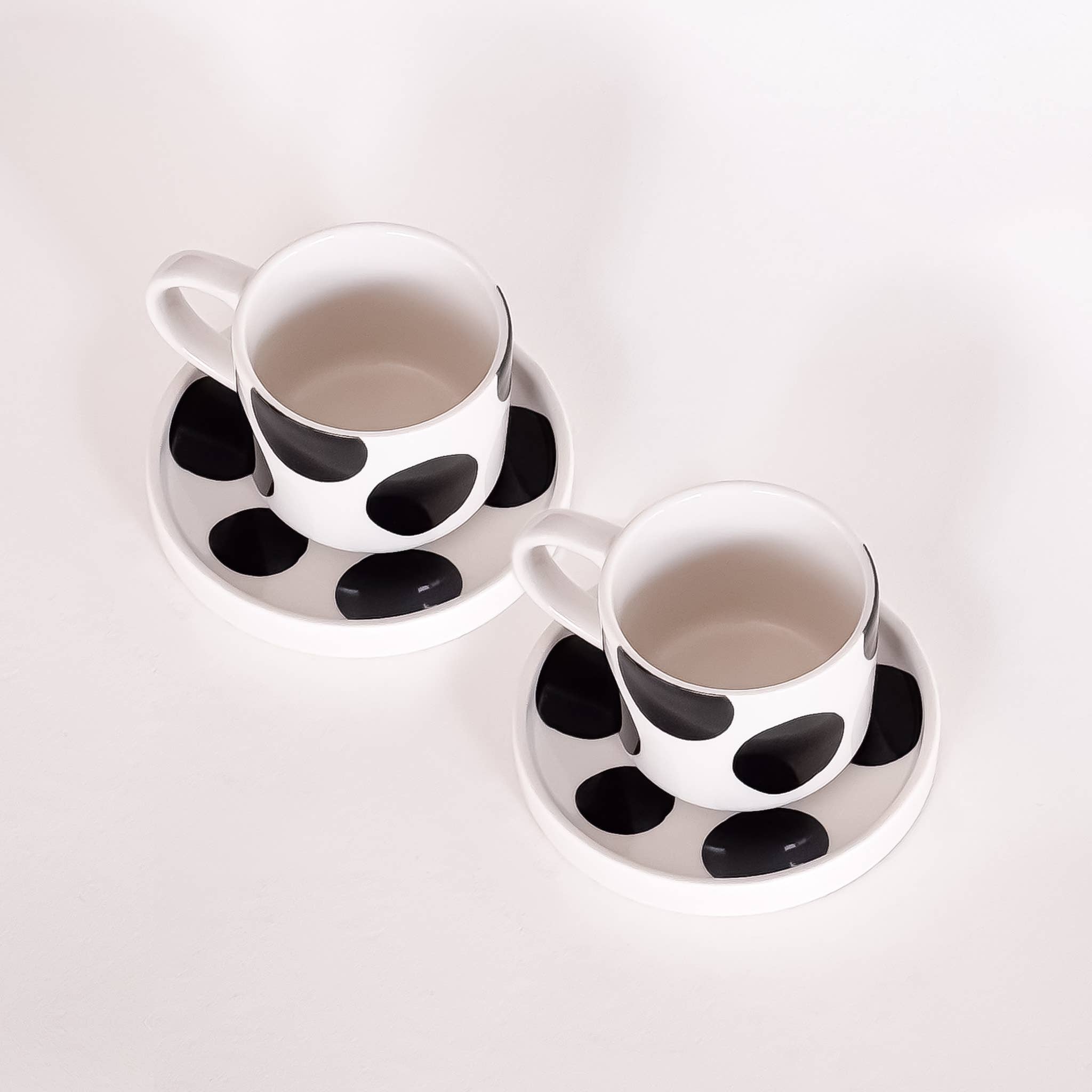 twee witte met zwarte stippen kop en schotels voor espresso op een witte achtergrond