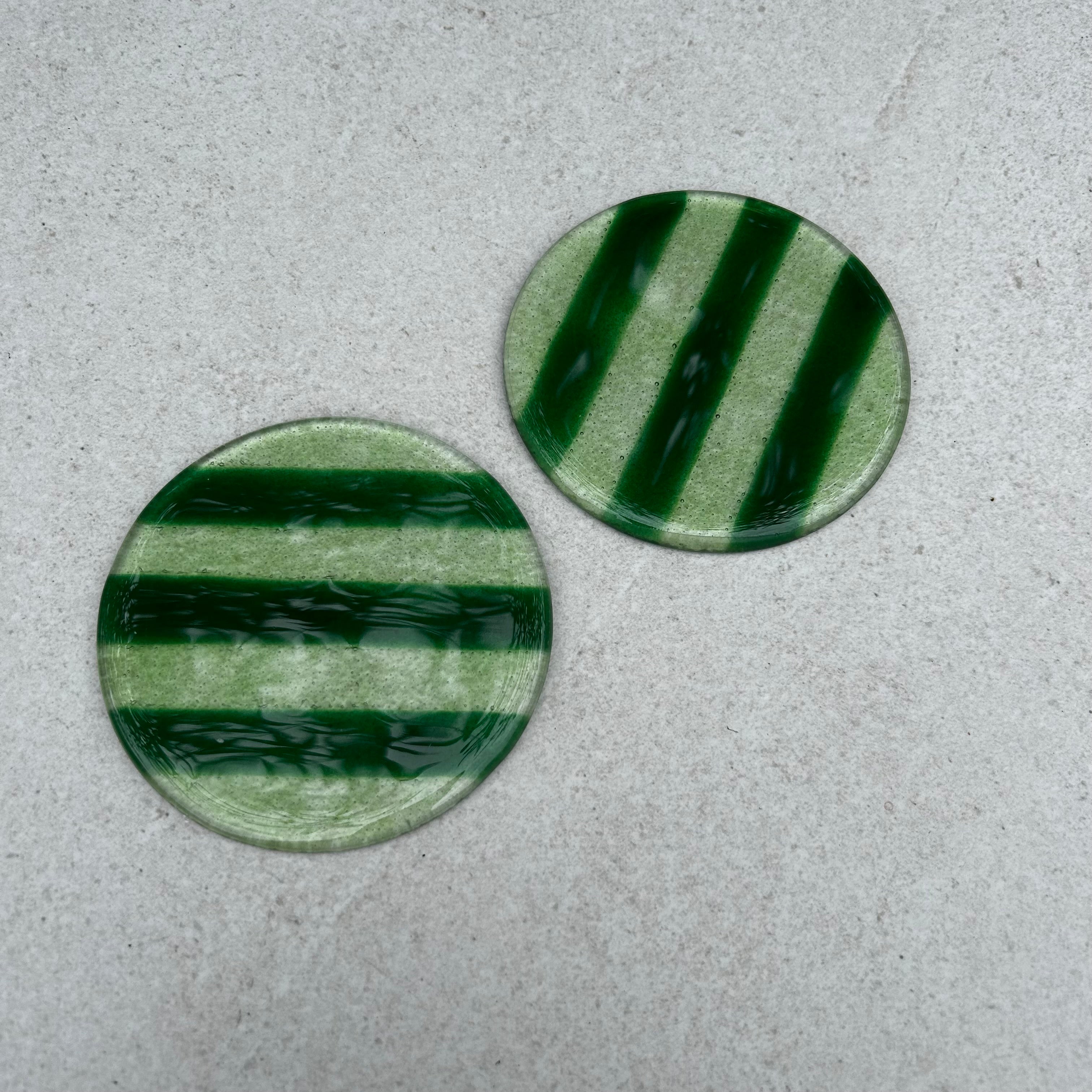 Bovenaanzicht twee glazen ronde onderzetters met groene strepen op een beige achtergrond.