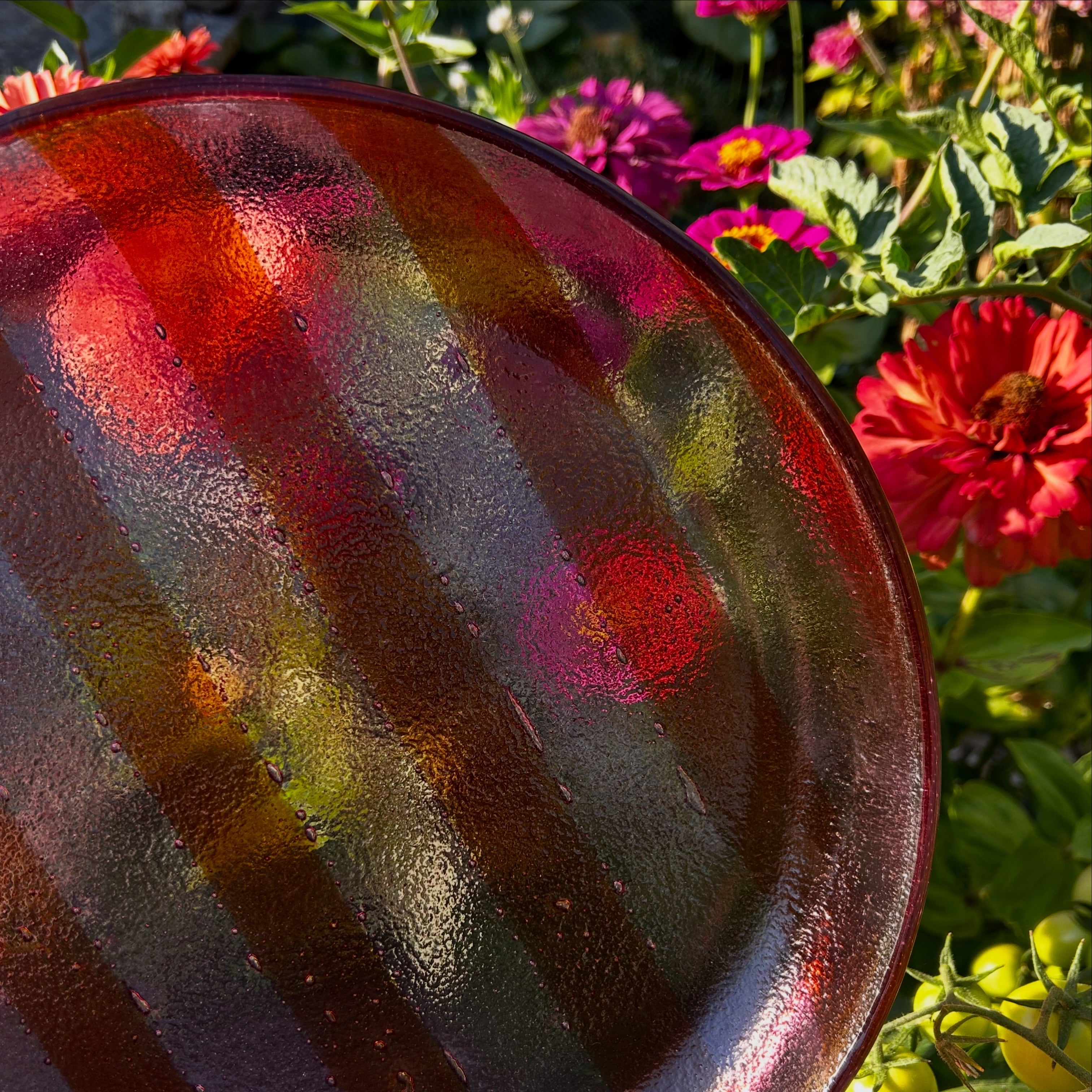 Vooraanzicht van een ronde glazen serveerschaal met oranje en roze strepen voor een bloemenachtergrond.