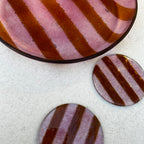 Bovenaanzicht van een ronde roze glazen serveerschaal met oranje strepen en 2 ronde glazen onderzetters, roze met oranje strepen op een witte achtergrond.