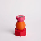 Kandelaar met verwisselbare componenten in de kleuren roze, oranje en rood.