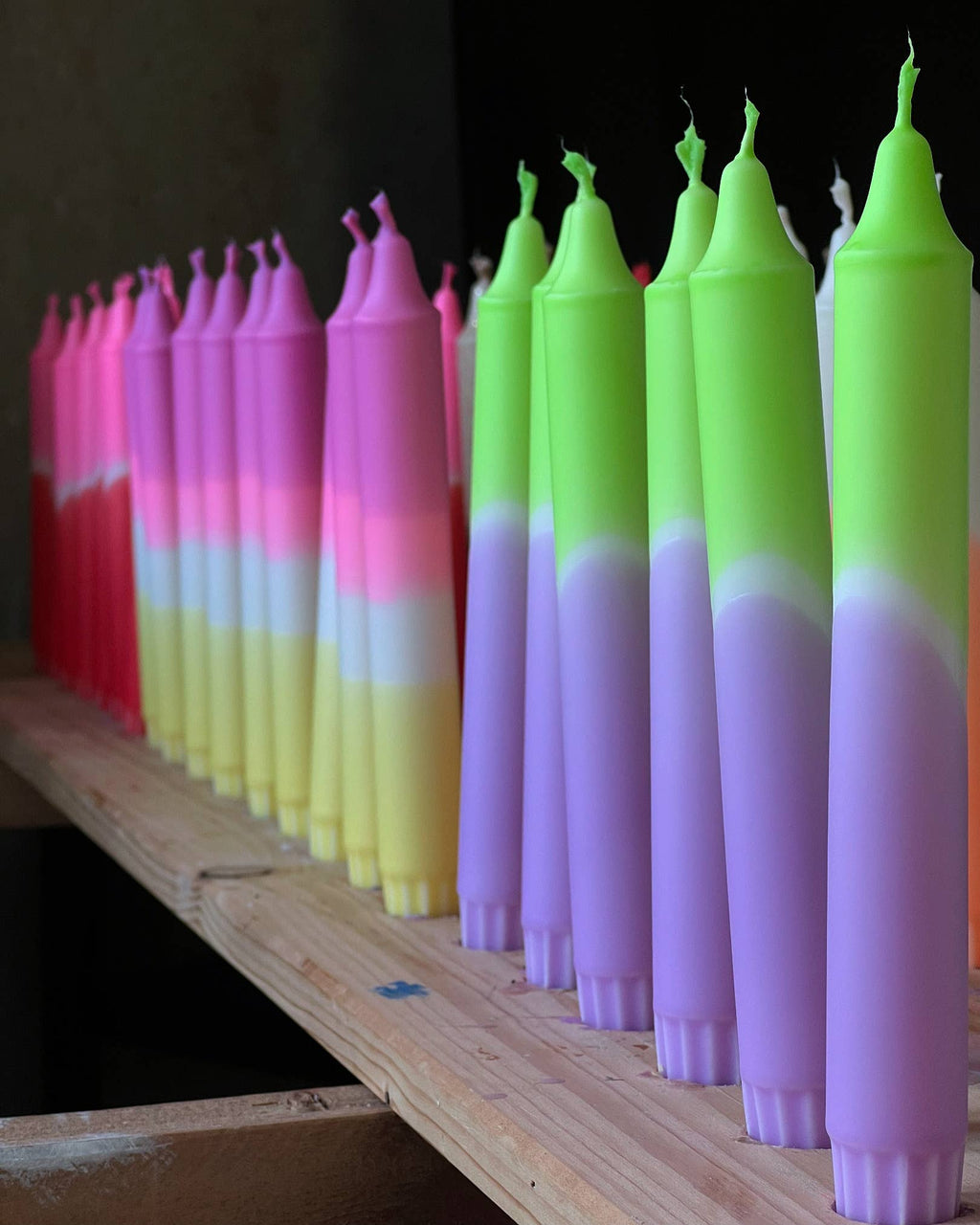 Display met verschillende handgemaakte dip dye kaarsen in felle kleuren op een houten plank.