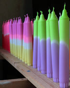 Display met verschillende handgemaakte dip dye kaarsen in felle kleuren op een houten plank.