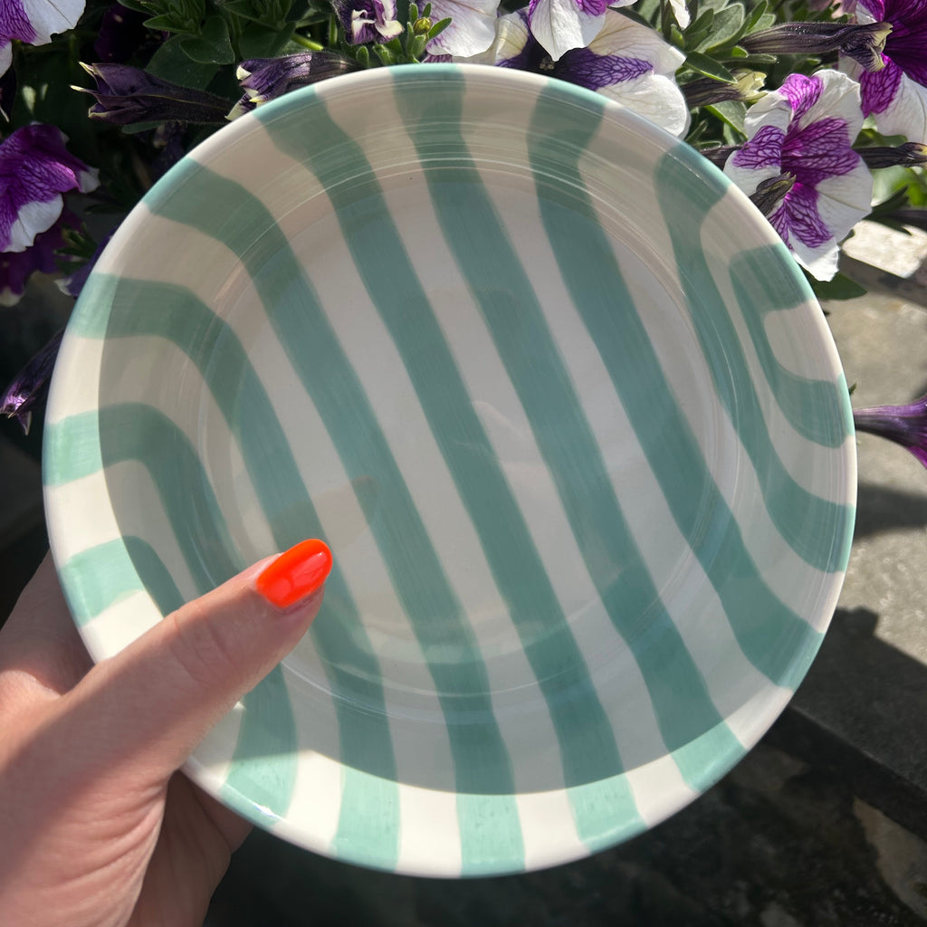 Schaaltje met mintgroene en witte strepen met bloemen op de achtergrond. Bovenaanzicht.