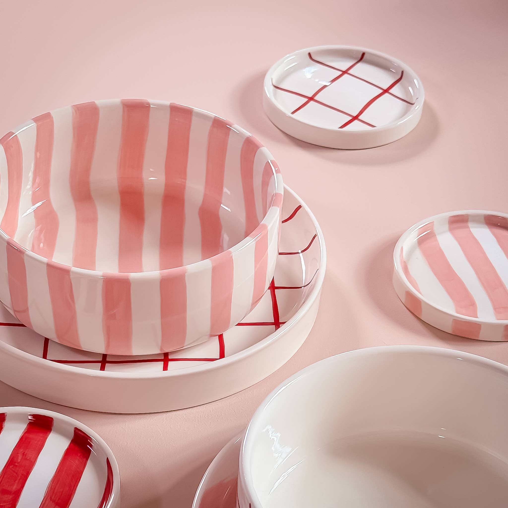 Divers servies van Magazin Minori in rood en roze met verschillende patronen op een lichtroze achtergrond.