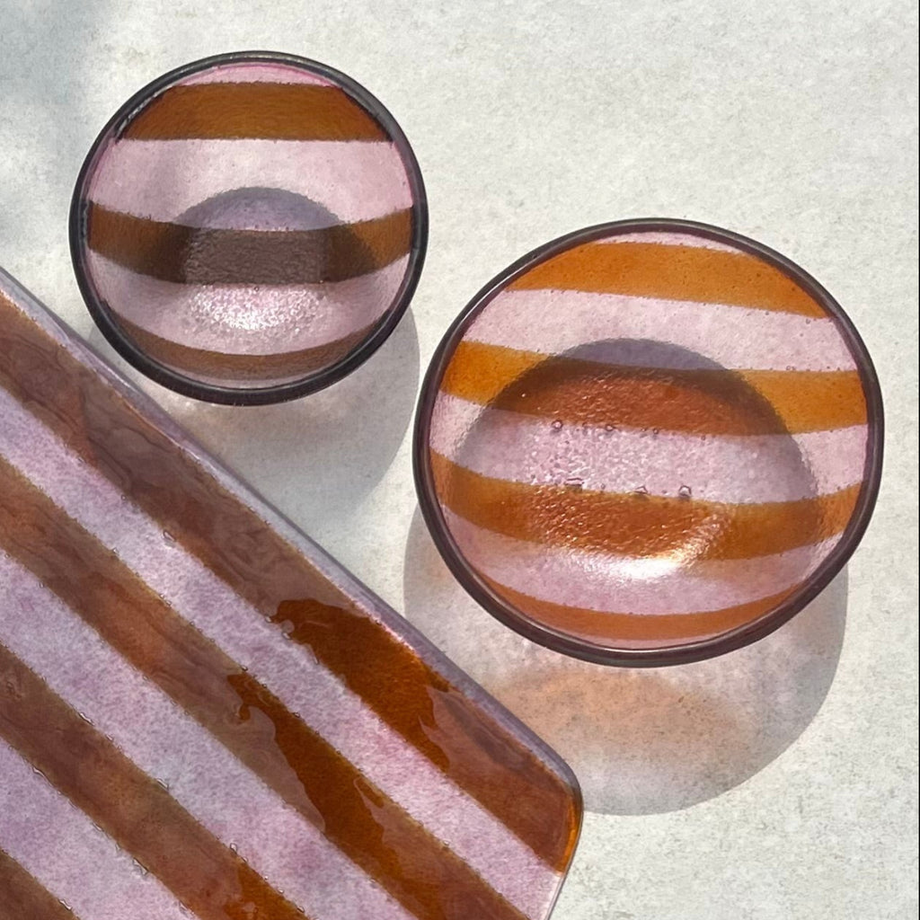 Bovenaanzicht van twee schaaltjes van glas met roze strepen in de maten S en XS op een beige achtergrond.