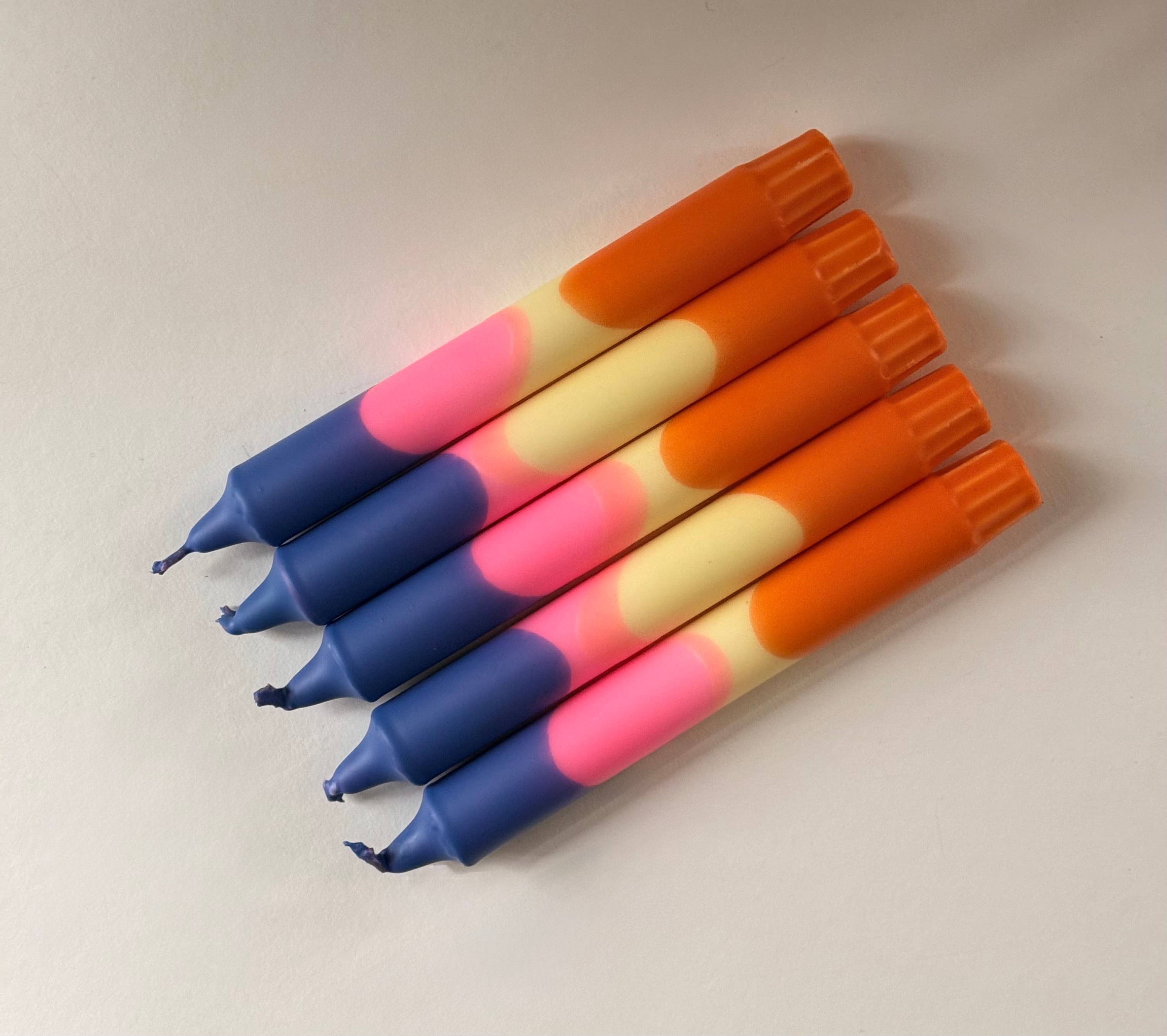 5 handgemaakte kaarsen met kleurenverloop in blauw, roze, geel en oranje op een witte achtergrond.