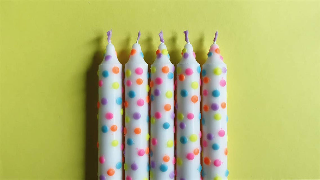 5 Witte handgemaakte dip dye kaarsen met confetti stippen in pastel kleuren op een gele achtergrond