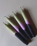 4 dip dye kaarsen met kleurverloop in olijfgroen, paars en donkerblauw op een beige achtergrond