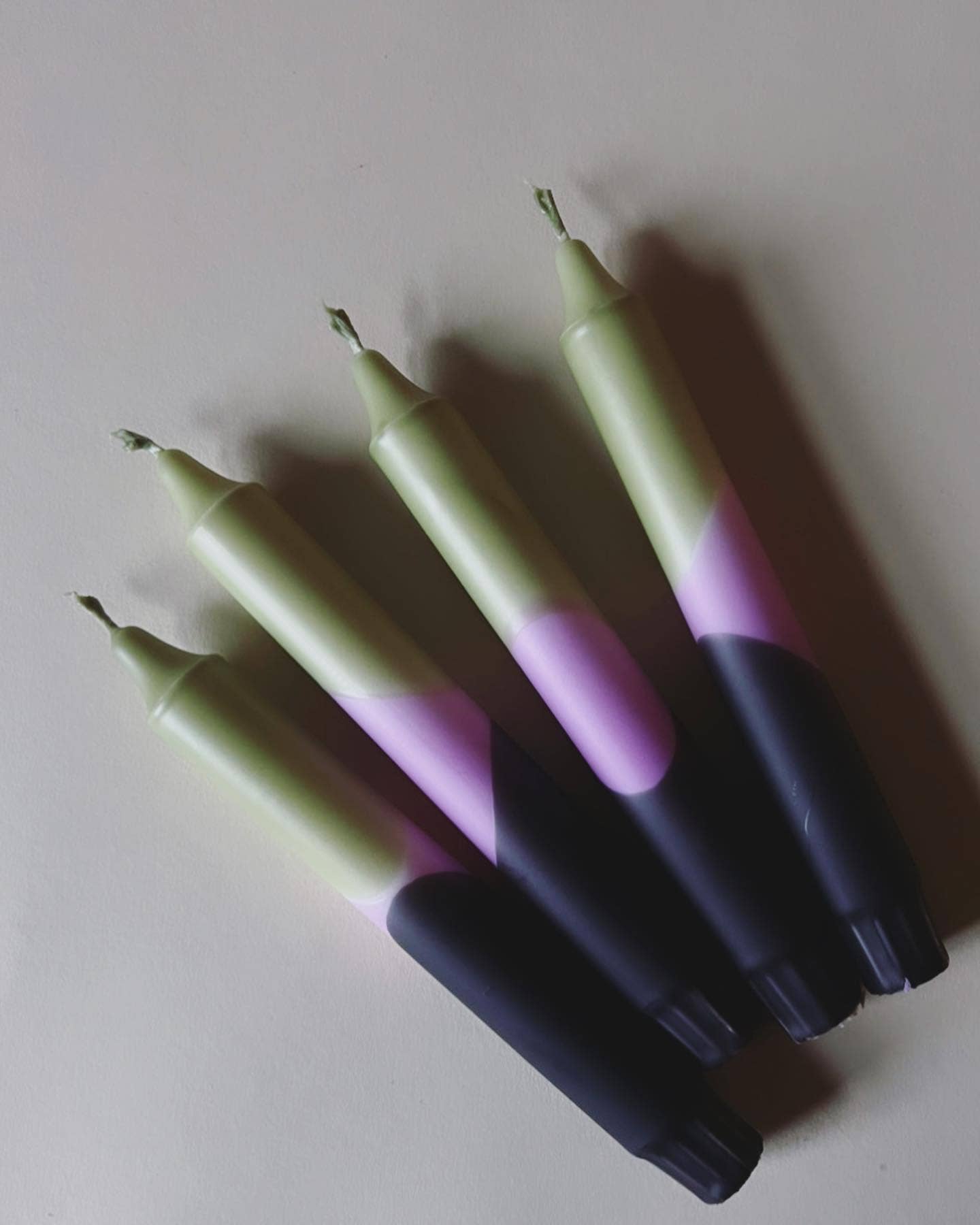 4 dip dye kaarsen met kleurverloop in olijfgroen, paars en donkerblauw op een beige achtergrond